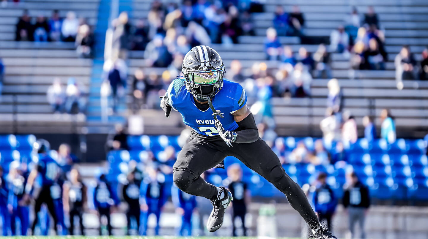 A football player in a blue jersey and black pants sprints across the field during a game.